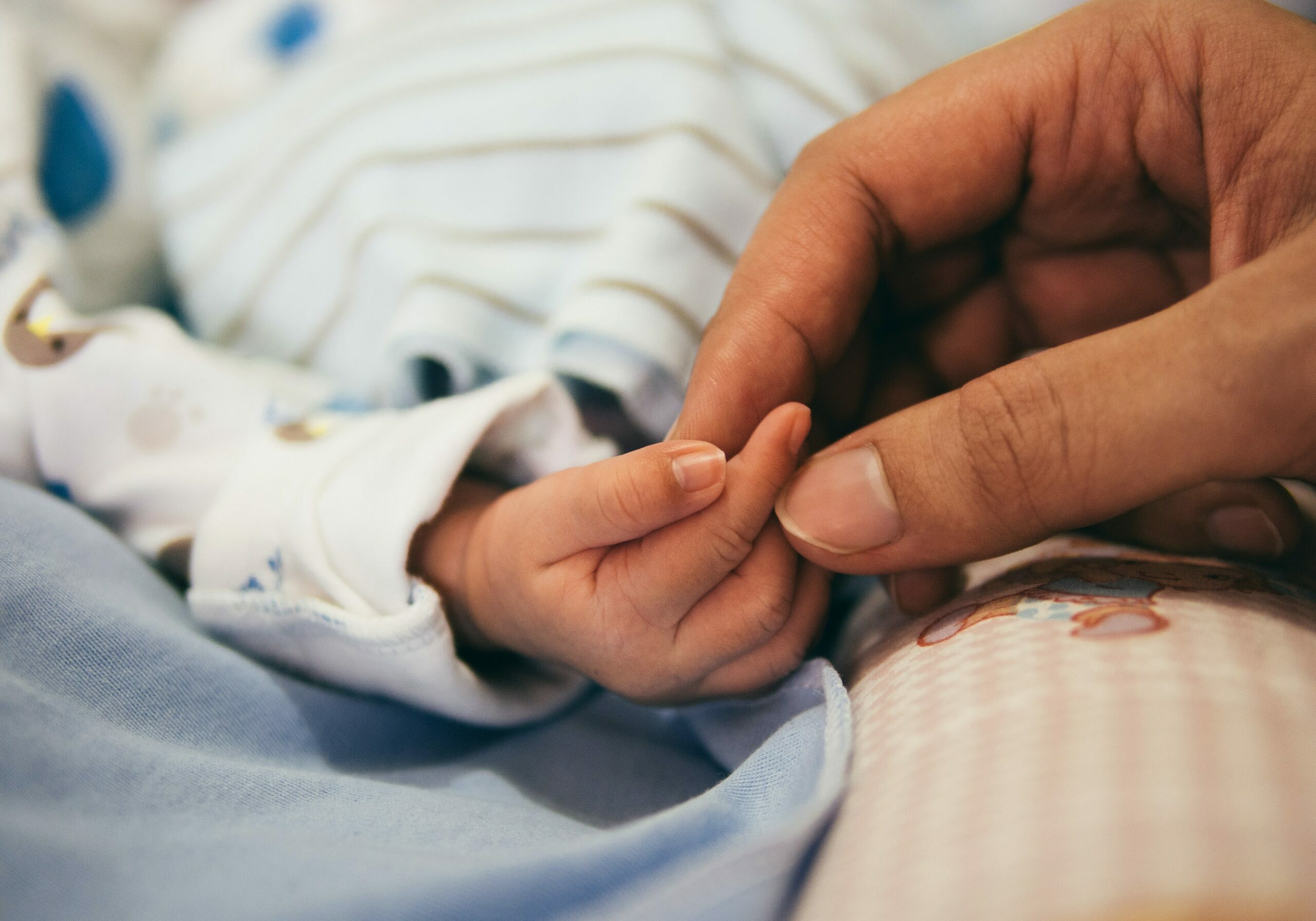 A mother's hand holding the small hand of her newborn baby.