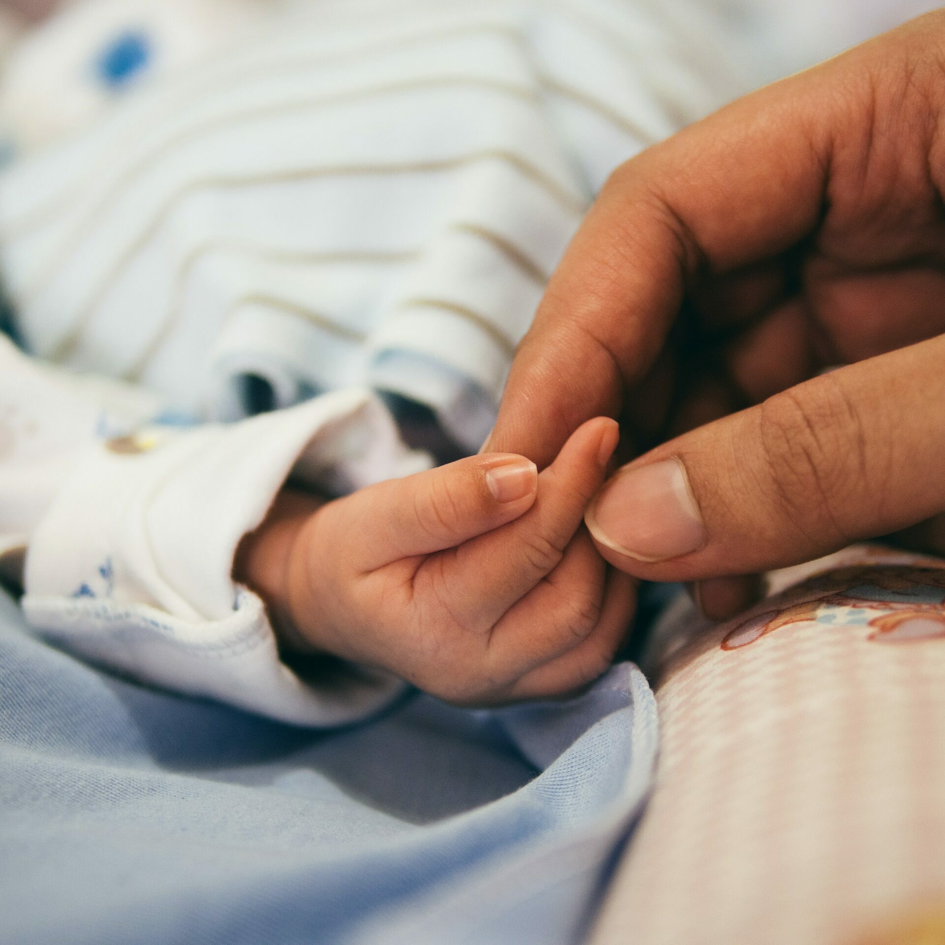 A mother's hand holding the small hand of her newborn baby.