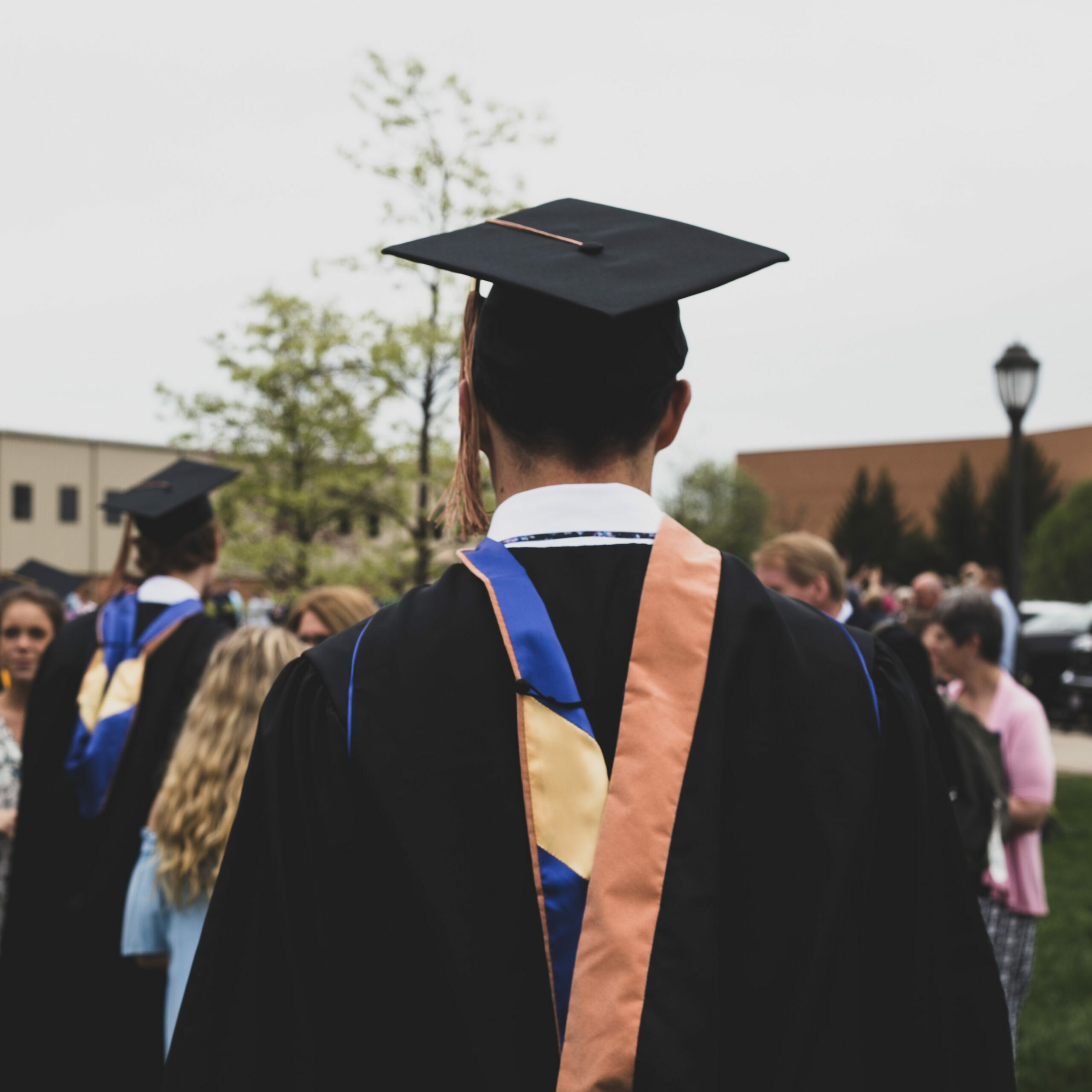 A young college graduate, standing in the garden along with other graduates and family members.