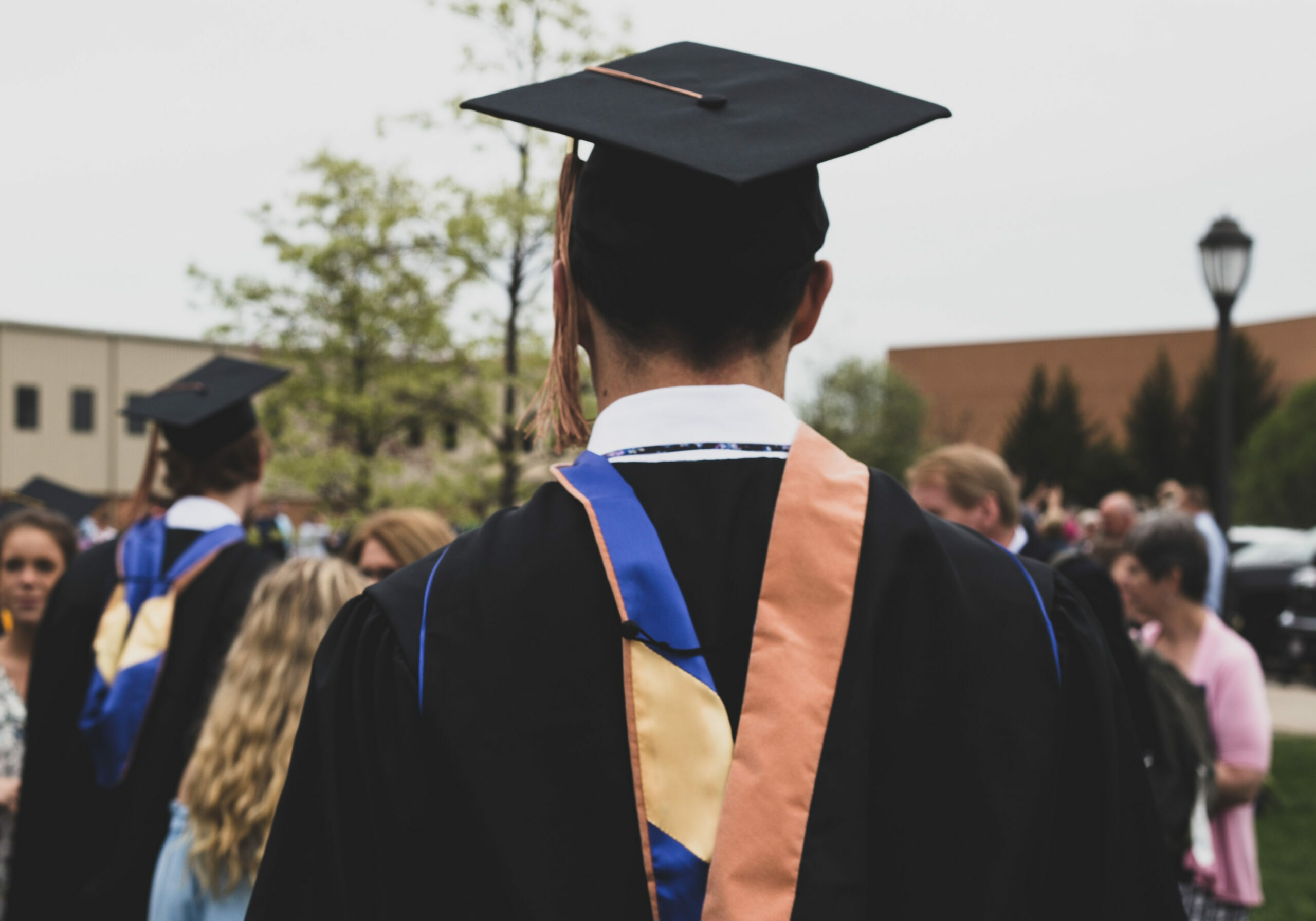 A young college graduate, standing in the garden along with other graduates and family members.