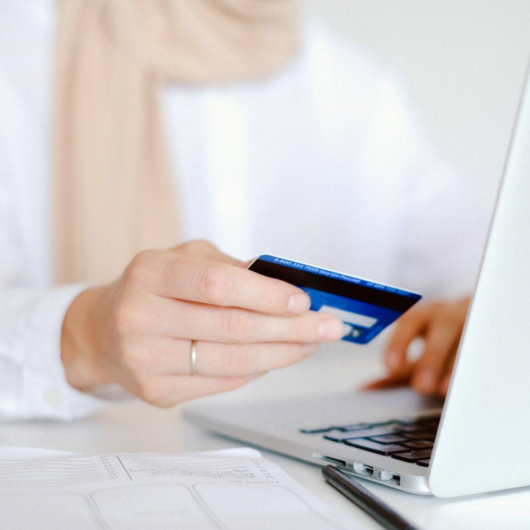 A woman holds her credit card in her hand while entering a payment on a laptop.