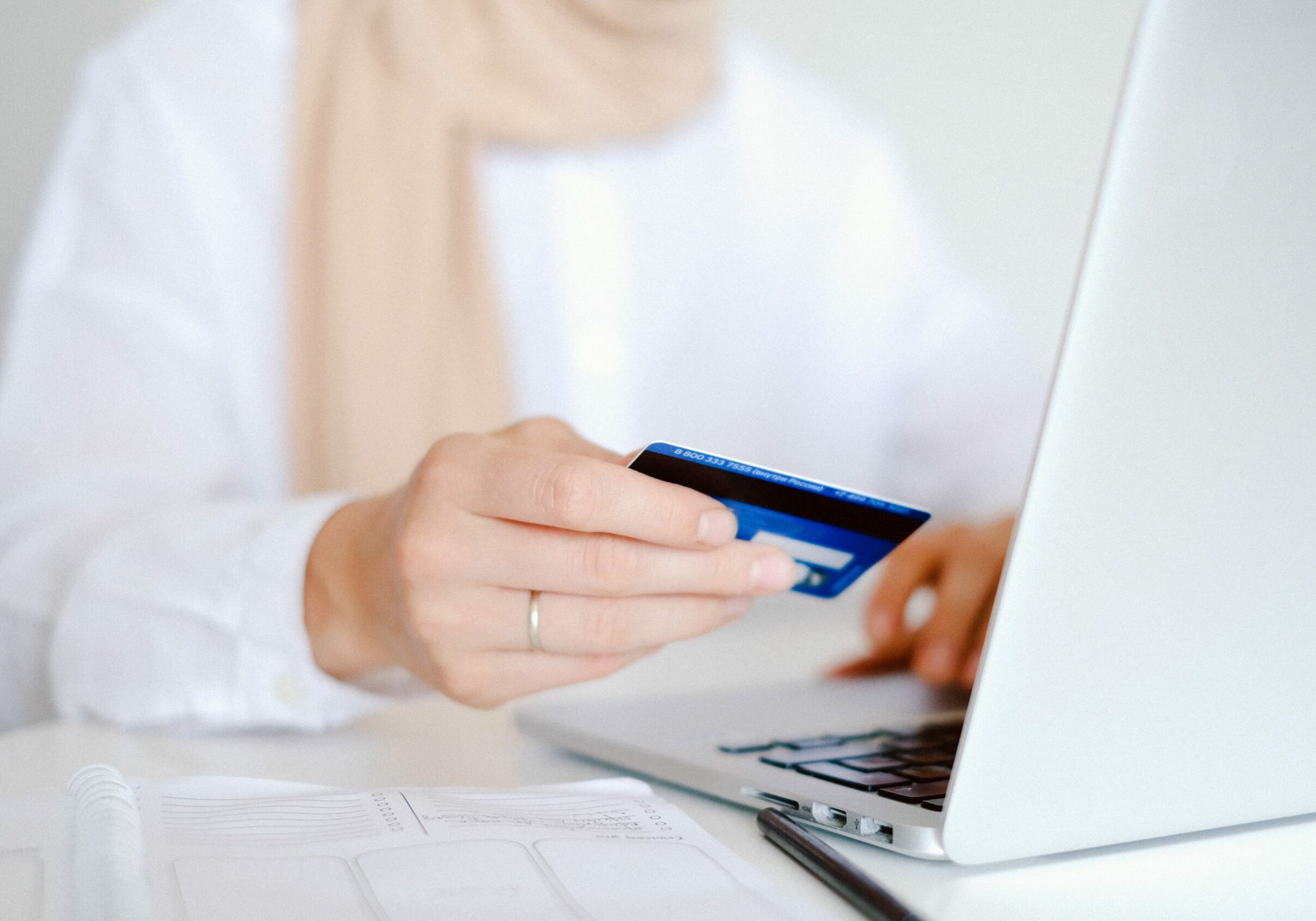 A woman holds her credit card in her hand while entering a payment on a laptop.