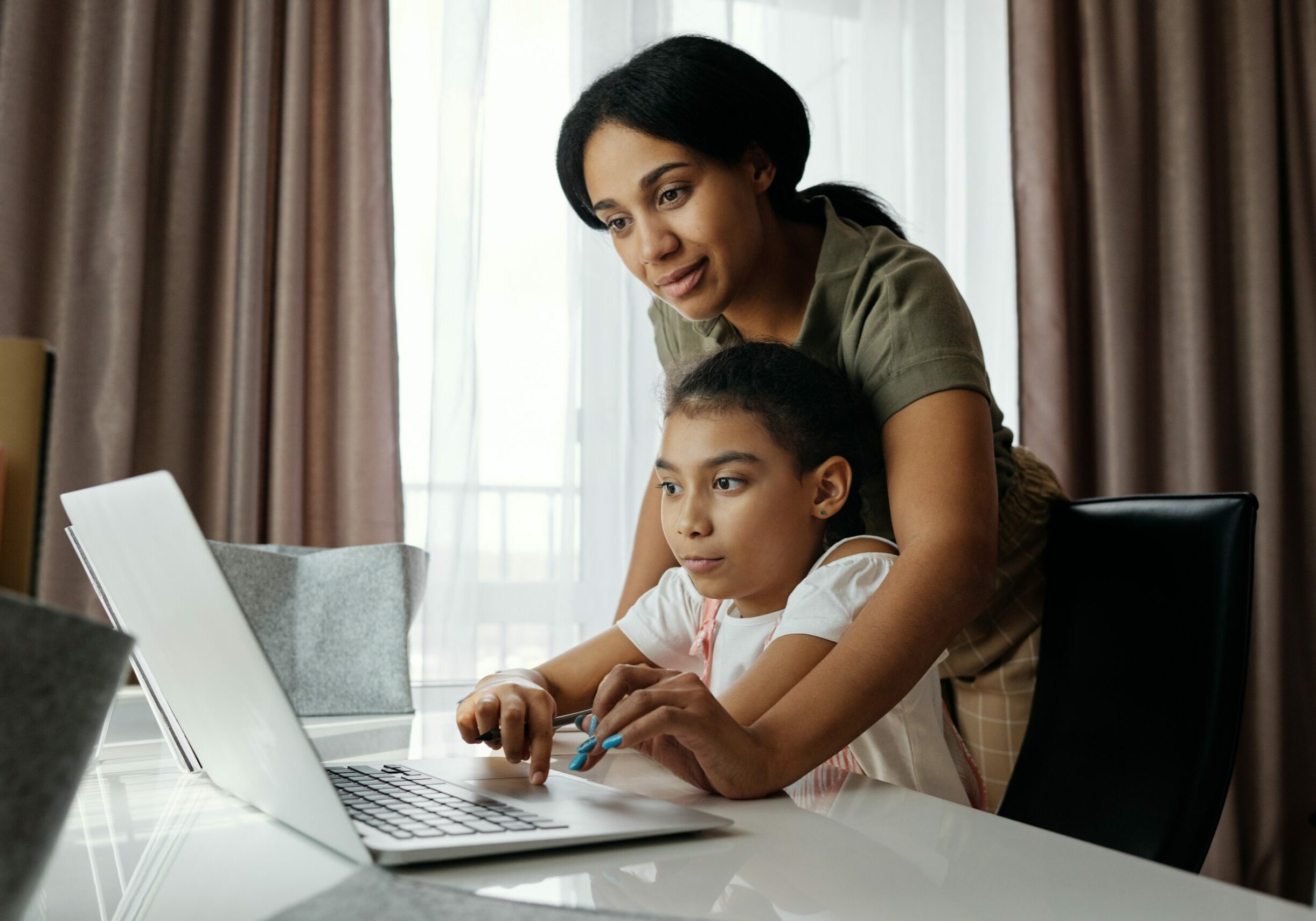 Mom and daughter in the dining room doing homework on a laptop.