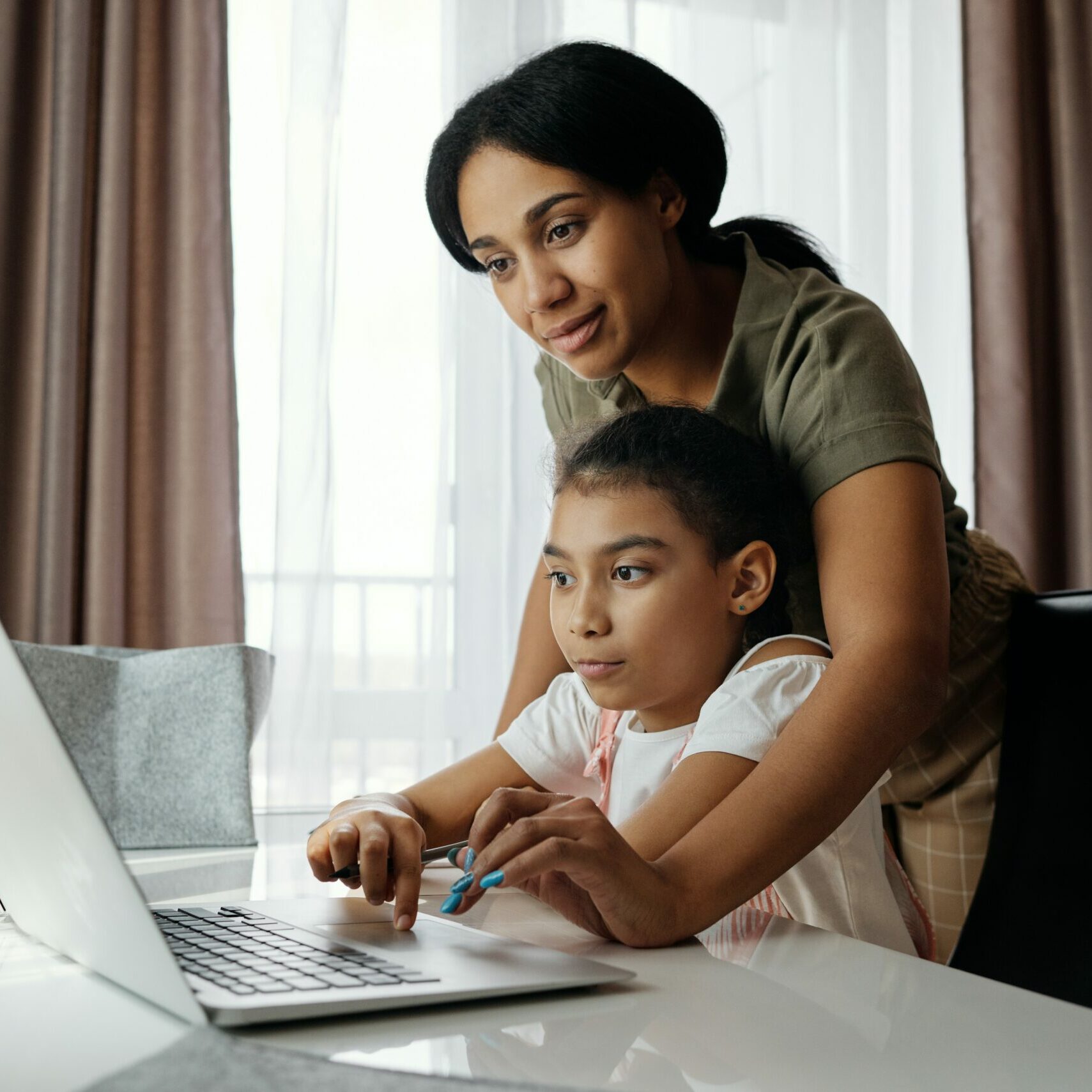 Mom and daughter in the dining room doing homework on a laptop.