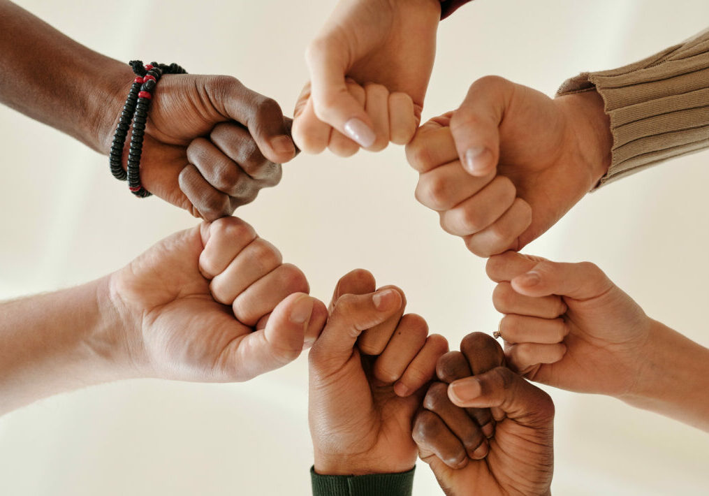 Seven hands, with clenched fists, joining to create a circle of union.