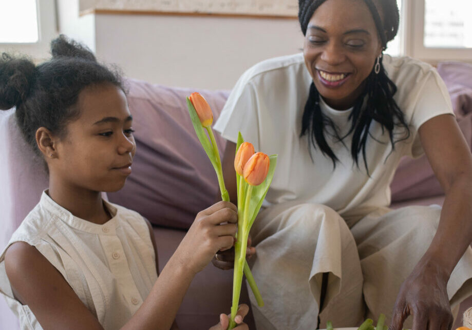 A single mother and her daughter, smiling and sitting in the living room, creating a flower arrangement.