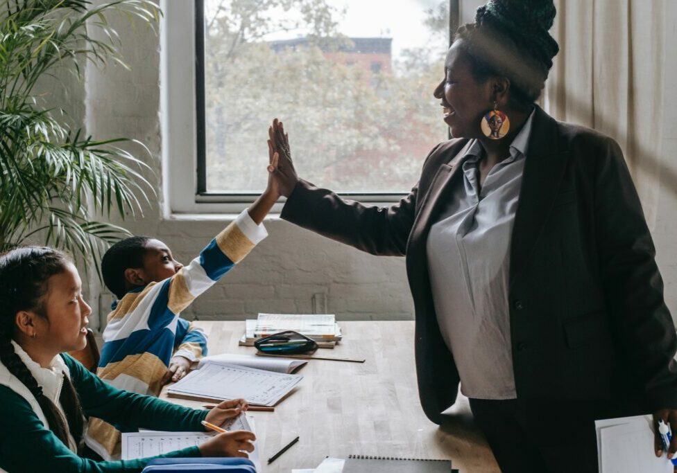 Two students sitting on a bench, one of them high-fiving the teacher.