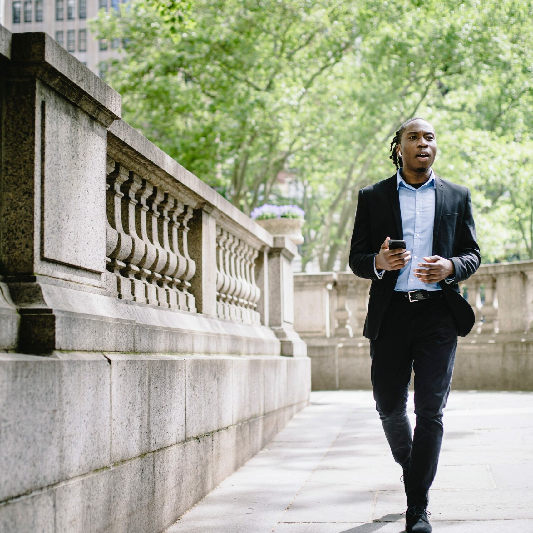 A young adult walking down the street in his suit, going to work happy and listening to music.