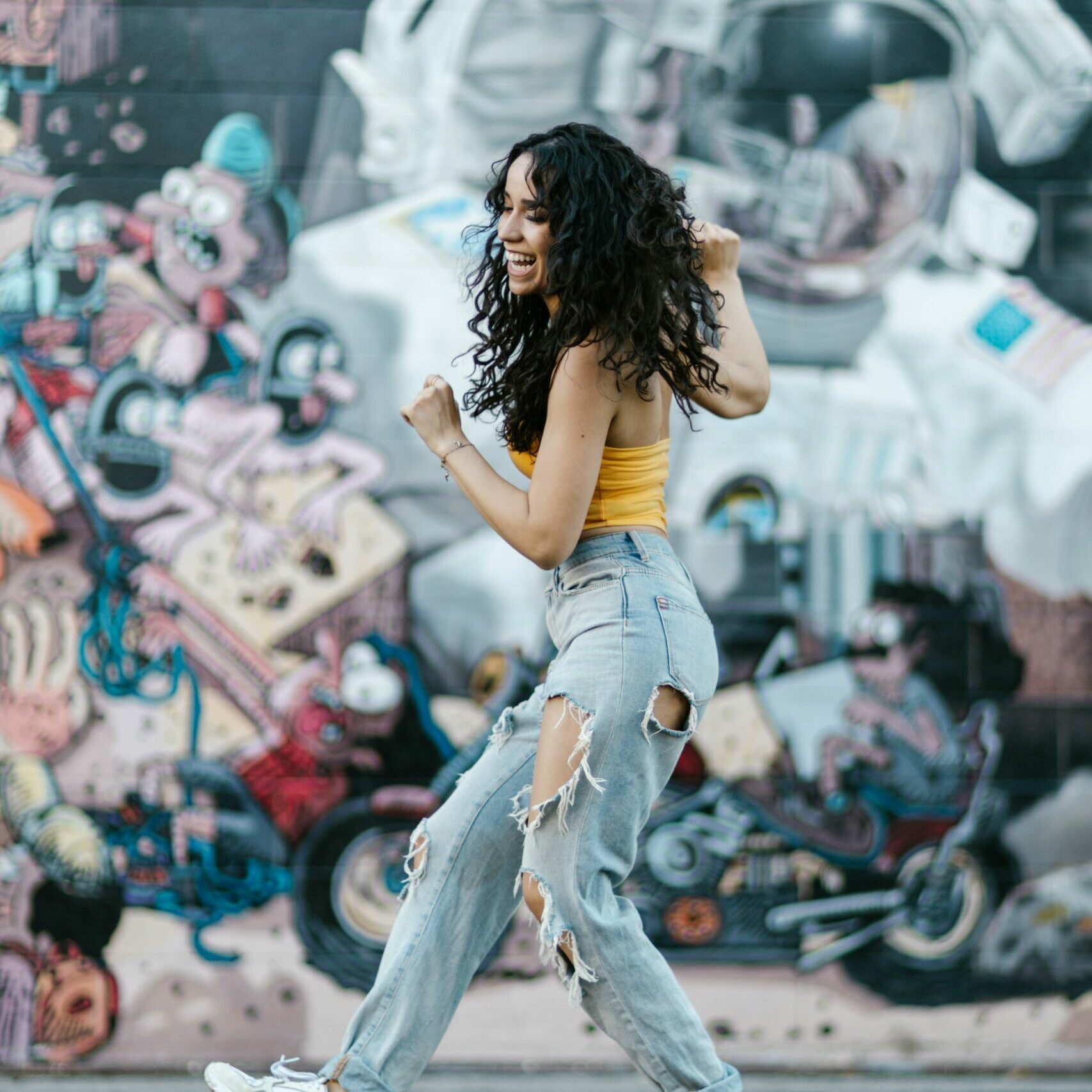 A girl who is walking and dancing in the street is happy and smiling.