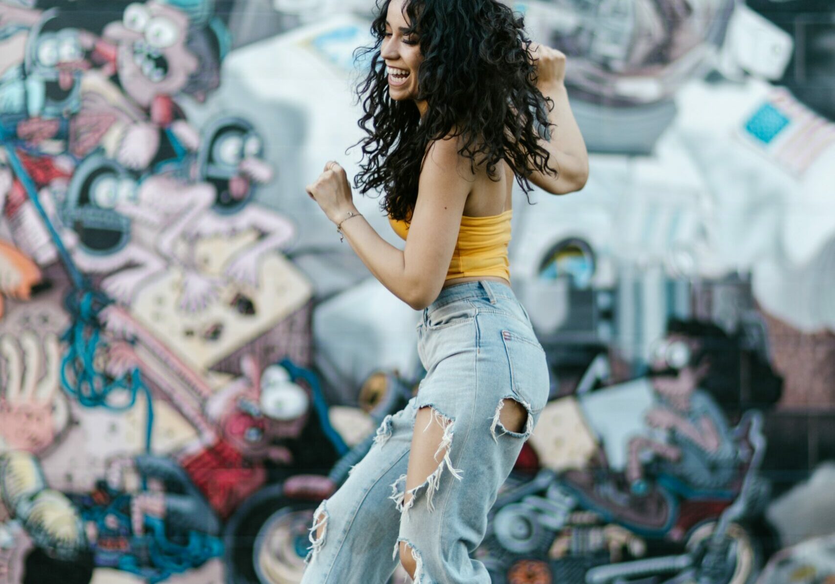 A girl who is walking and dancing in the street is happy and smiling.